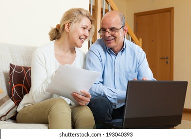 Happy mature couple with financial documents and notebook in home interior
