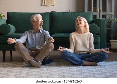 Happy mature couple having fun, practicing yoga together at home, laughing grey haired man and woman sitting in lotus pose on floor in living room, breathing, relaxing, healthy lifestyle concept - Powered by Shutterstock