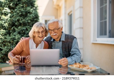 Happy Mature Couple Having Video Call Over Laptop While Relaxing On Nursing Home Patio. 