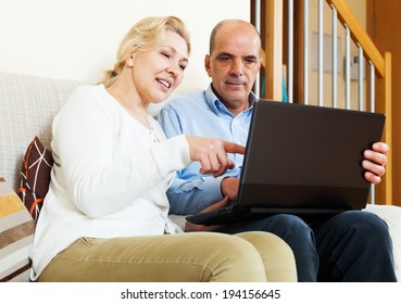 Happy mature couple with laptop at table at home