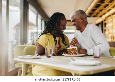 Happy mature couple laughing cheerfully while sharing a delicious cake in a cafe. Carefree senior couple having a good time in a restaurant. Mature couple enjoying their retirement together.