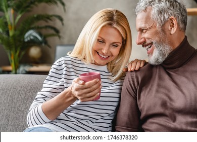 Happy mature couple laughing and drinking coffee while having fun at home