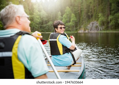 Happy mature couple in life vests canoeing in forest lake. Sunny summer day. Tourists traveling in Finland, having adventure. 