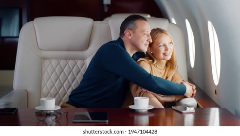 Happy Mature Couple Looking Through Window In Airplane First Class. Rich Married Man And Woman Relaxing In Private Jet Enjoying Travelling Together By Plane