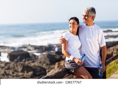 Happy Mature Couple Relaxing After Exercise At The Beach
