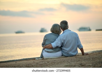 Happy Mature couple relaxing on beach at sunset,back view