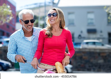 Happy Mature Couple Riding Bicycle On City Street