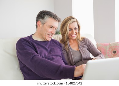 Happy Mature Couple Sitting On A Sofa And Looking At Laptop