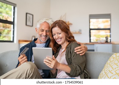 Happy mature couple sitting on sofa and doing online shopping on digital tablet. Senior husband and smiling wife paying bills online. Middle aged couple doing online payment on laptop, copy space. - Powered by Shutterstock