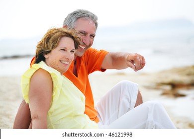 Happy Mature Couple Sitting On The Beach.