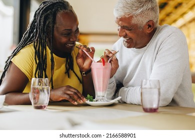 Happy mature couple smiling at each other while sharing a delicious milkshake. Cheerful senior couple having a good time in a restaurant. Carefree mature couple enjoying their retirement together. - Powered by Shutterstock
