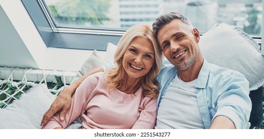 Happy mature couple smiling and looking at camera while relaxing at home together - Shutterstock ID 2251543277