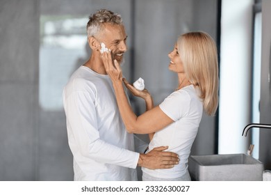 Happy Mature Couple Spending Time In Bathroom Together, Caring Wife Applying Shaving Foam On Husband's Face And Laughing, Romantic Senior Spouses Making Beauty Routine At Home, Free Space - Powered by Shutterstock