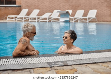 happy mature couple in sunglasses chatting inside of swimming pool during vacation, wellness retreat - Powered by Shutterstock