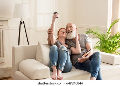 Happy mature couple taking selfie while sitting on sofa at home - Powered by Shutterstock