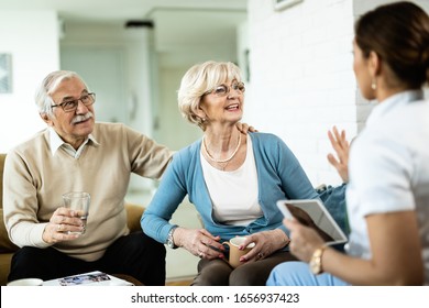 Happy Mature Couple Talking To Female Nurse Who Is Visiting Them At Home. 