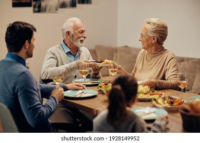 Happy Mature Couple Talking While Having Family Lunch And Passing Food At Dining Table. 