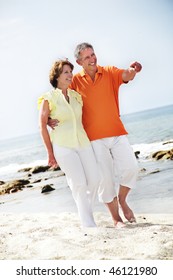 Happy Mature Couple Walking Along The Beach.