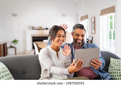 Happy mature couple waving hands while making online video call with digital tablet. Mid adult multiethnic man and latin woman doing video call with family from home with copy space.  - Powered by Shutterstock