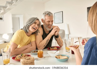 Happy mature family couple having breakfast with teen daughter sit at kitchen table. Cheerful older mid age parents having fun talking, eating toasts and waffles enjoying morning meal together. - Powered by Shutterstock