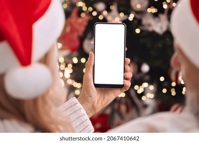 Happy mature family couple in santa hats holding smartphone in hands using cell phone mockup white blank screen for ads on Christmas tree background advertising mobile applications. Over shoulder view - Powered by Shutterstock