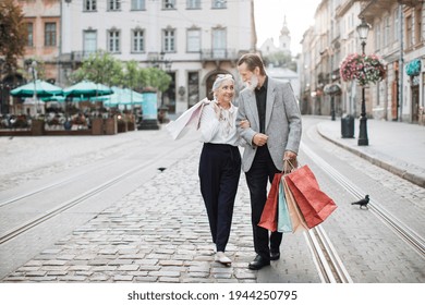 Happy mature family walking in embrace on city street with shopping bags in hands. Lovely couple smiling and looking on each other. Time together. - Powered by Shutterstock