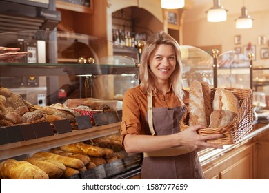 Happy mature female baker holding basket of bread, working at her bakery store. Middle aged female entrepreneur selling homemade bread - Powered by Shutterstock