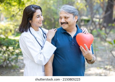 Happy mature female indian doctor standing with senior male patient holding red heart shape balloon, both standing outdoor in the park, healthcare profession. cardiology. - Powered by Shutterstock