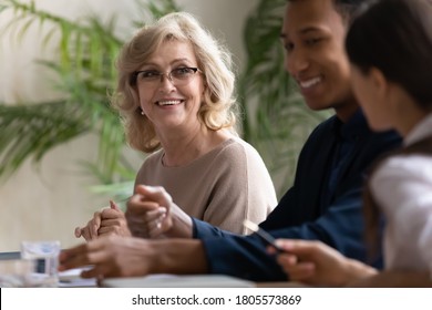 Happy Mature Female Manager Listening To Diverse Young Colleagues, Satisfied With Working Results At Office Meeting. Smiling Motivated Different Generations Multiracial Teammates Developing Project.