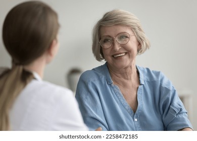 Happy mature female patient consulting doctor in office, talking to physician, discussing healthcare medical examination, smiling, laughing. Older insurer woman listening therapy recommendation - Powered by Shutterstock