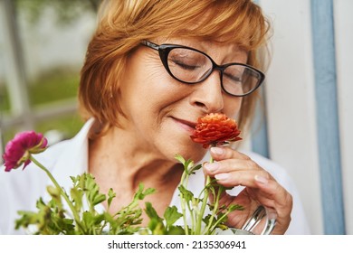 Happy Mature Female Smelling Flowers In Countryside