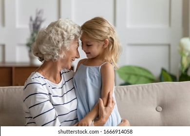 Happy Mature Grandmother Hug Embrace Enjoy Family Moment With Cute Little Preschooler Granddaughter, Smiling Senior Granny Cuddle Have Fun Play With Small Girl Child In Living Room