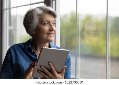Happy mature grey-haired Caucasian woman use modern tablet gadget look in window distance thinking. Smart senior 60s grandmother browse internet on pad device at home. Elderly and technology concept. - Powered by Shutterstock