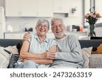 Happy mature husband and wife sit rest on couch at home hugging and cuddling, show care affection, smiling senior loving couple relax on sofa have fun, enjoy tender romantic family weekend together