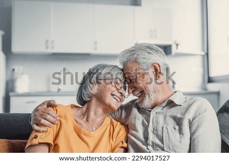 Happy mature husband and wife sit rest on couch at home hugging and cuddling, show care affection, smiling senior loving couple relax on sofa have fun, enjoy tender romantic family weekend together