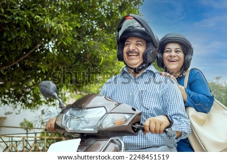 Happy mature indian couple wearing helmet riding motor scooter on road. Retirement life, Adventure and travel, Closeup, low angle shot.