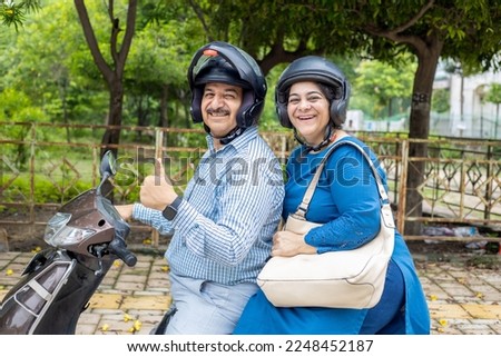 Happy mature indian couple wearing helmet riding motor scooter on road do thumbs up sign with hand. Retirement life, Adventure and travel, Closeup