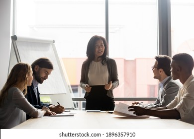 Happy mature korean asian female leader holding negotiations briefing meeting with motivated employees in modern office. Smiling skilled mixed race businesswoman mentoring colleagues near flipchart. - Powered by Shutterstock