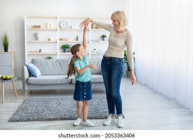 Happy mature lady and casual little daughter dancing waltz at home, standing in living room, full length photo. Loving grandmother teaching granddaughter how to dance having fun together at home - Powered by Shutterstock