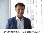 Happy mature male business leader head shot portrait. Confident middle aged 50s businessman, CEO, executive in formal suit looking at camera, smiling, standing at office window. Job success concept