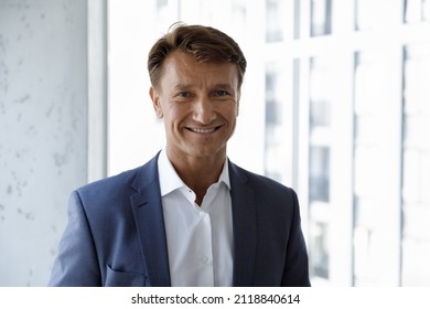 Happy mature male business leader head shot portrait. Confident middle aged 50s businessman, CEO, executive in formal suit looking at camera, smiling, standing at office window. Job success concept - Shutterstock ID 2118840614