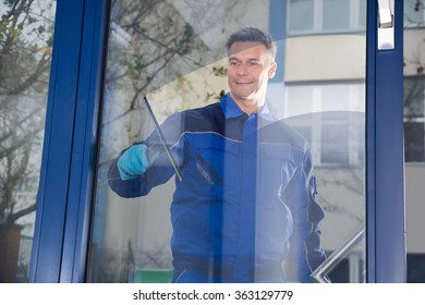 Happy mature male worker cleaning glass with squeegee