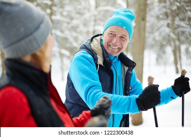 Happy Mature Man In Activewear Looking At His Wife While Skiing In Winter Forest At Leisure