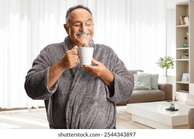 Happy mature man in a bathrobe enjoying a cup of hot steamy drink at home in a living room - Powered by Shutterstock