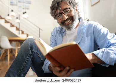 Happy mature man with glasses relaxing at home reading a book. Lifestyle concept. - Powered by Shutterstock