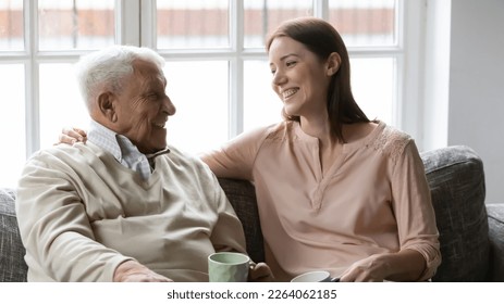 Happy mature man with grownup daughter having fun at home, chatting, talking, sharing news, sitting on cozy couch, smiling older father and young woman drinking tea coffee, enjoying leisure time - Powered by Shutterstock