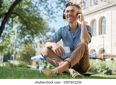 Happy mature man listening to music on headphones, relaxing in park