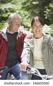 Happy Mature Man And Middle Aged Woman With Bikes In Forest