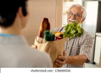 Happy mature man receiving groceries home delivery from a courier.  - Powered by Shutterstock