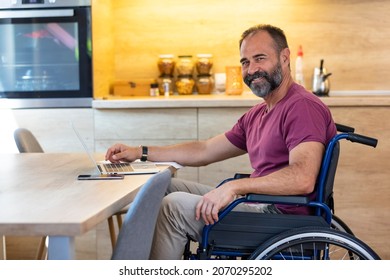 Happy Mature Man in wheelchair from home. Cheerful businessman smile while sitting in his wheelchair. Disabled Man in Wheelchair using Laptop At Home. Mature man sitting on wheelchair at the table. - Powered by Shutterstock